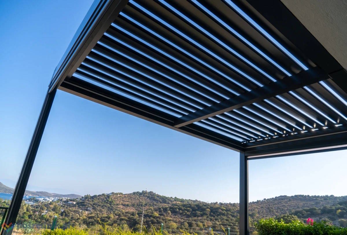 Dark aluminium louvred pergola with open slat roof overlooking countryside and blue sky