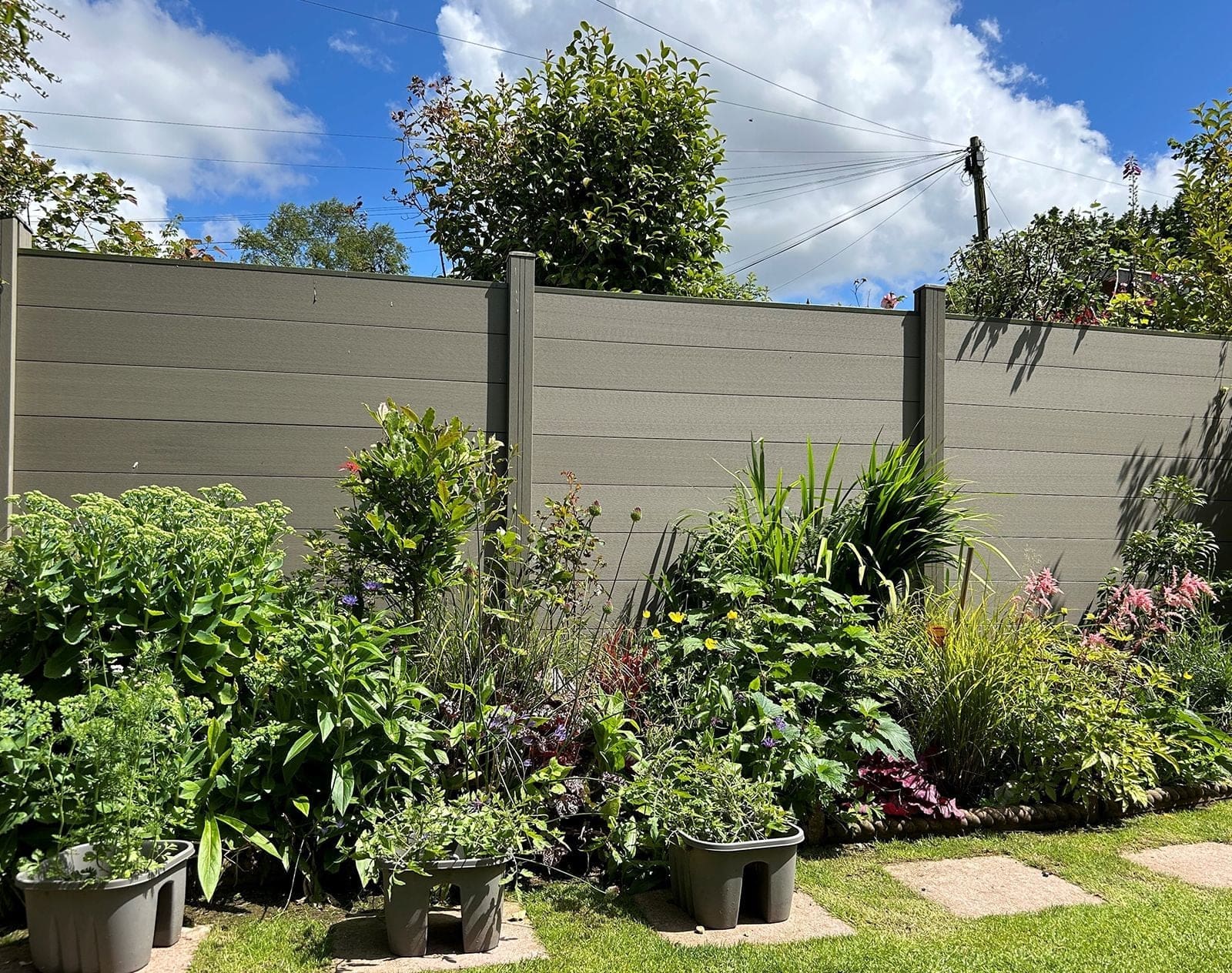 Grey composite fence panels with lush garden border planting and potted plants