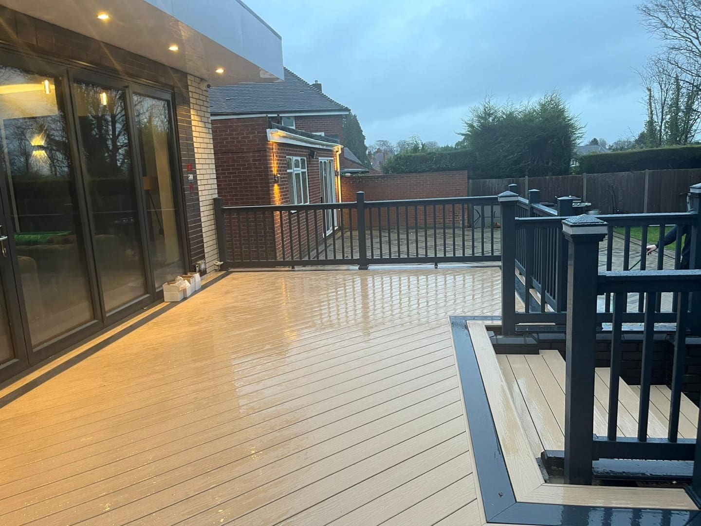 Light composite decking with black balustrade and steps leading to garden at dusk