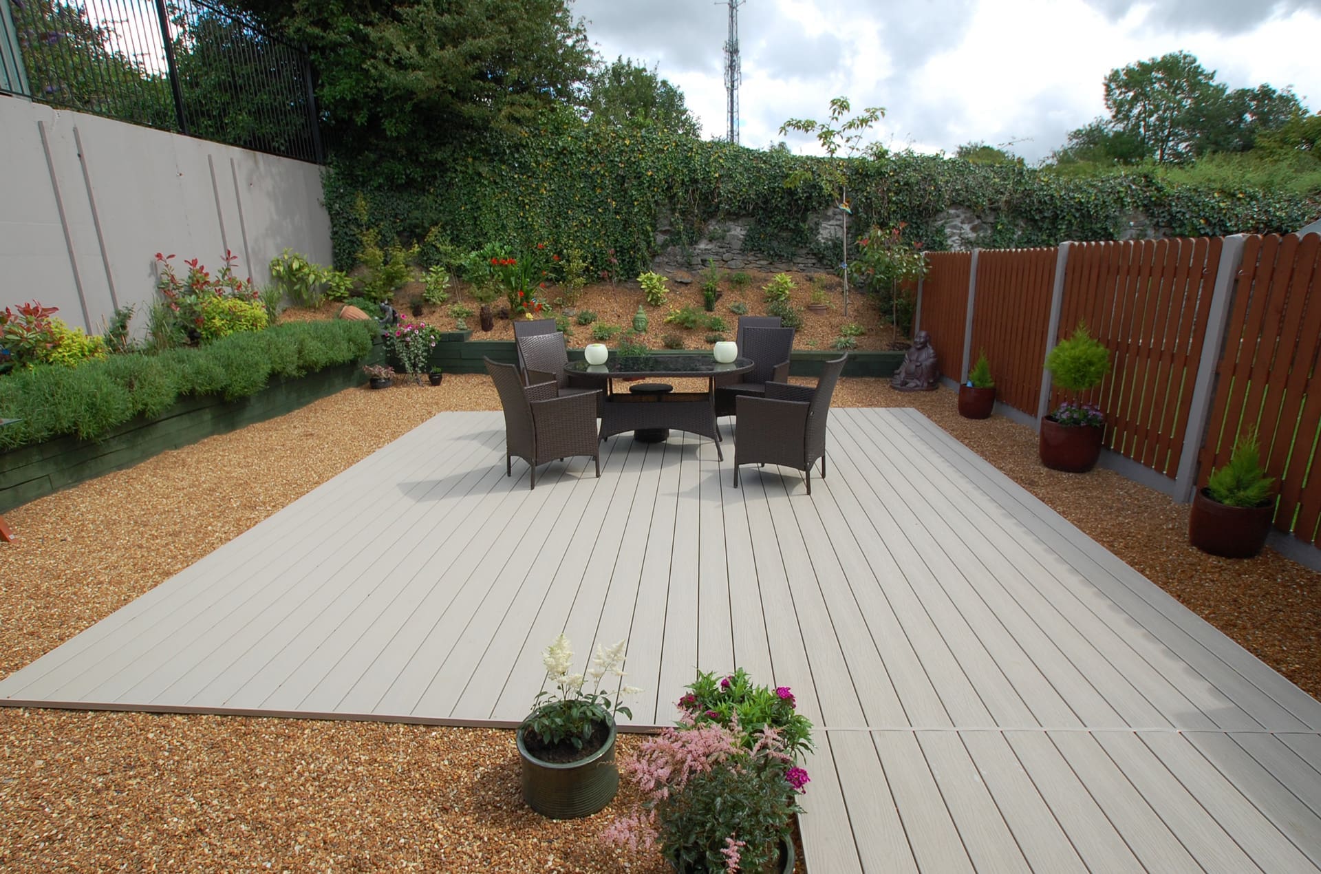 Light grey uPVC floating deck with rattan garden furniture surrounded by gravel and planting