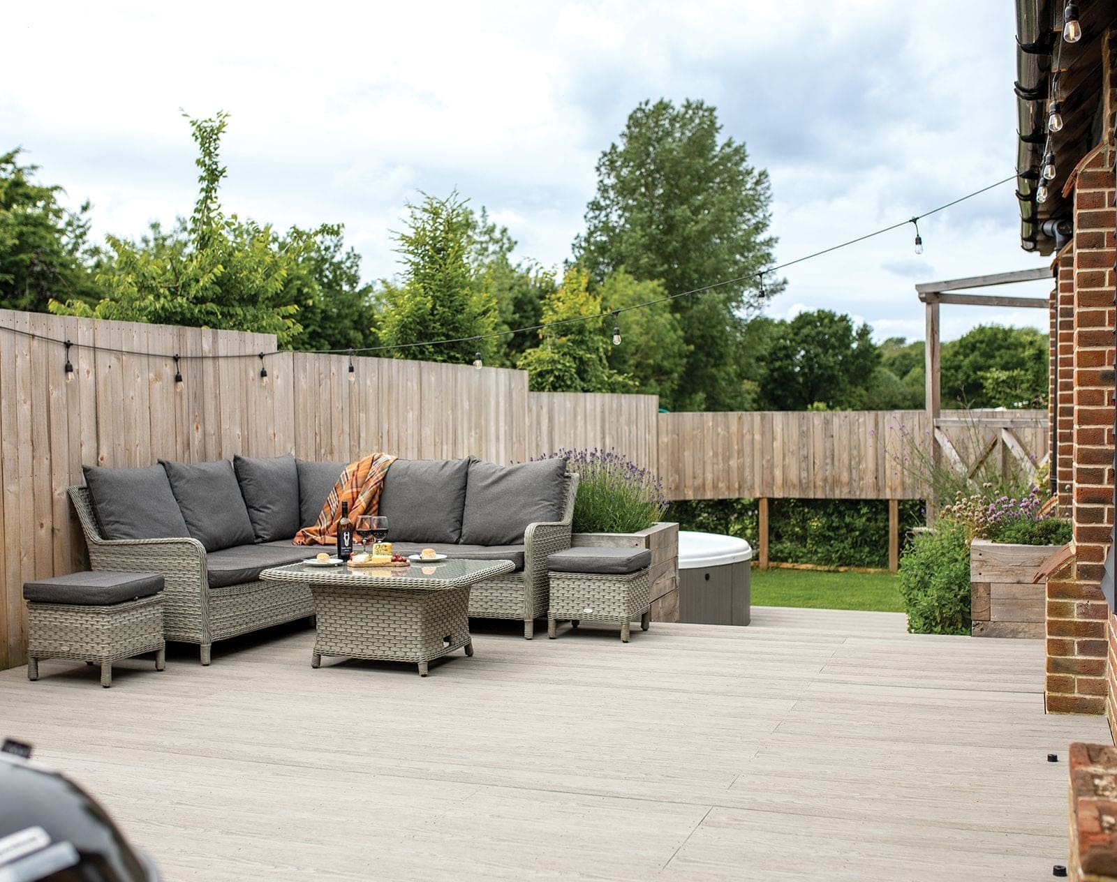 Pale grey Nordeck composite decking with rattan corner sofa set and festoon lighting