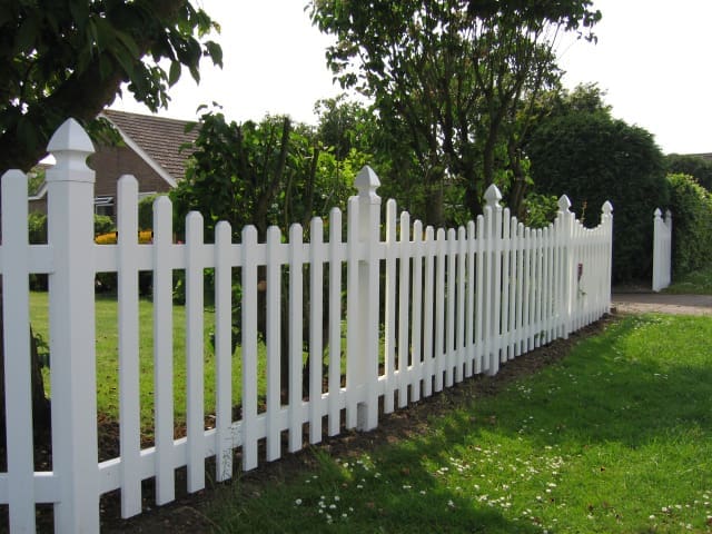 White uPVC Nantucket picket fence with decorative post caps bordering residential garden